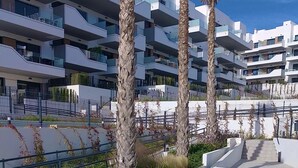 A modern residential building with balconies, a landscaped area with palm trees, and a rectangular water feature. - Luxe Appartement Orihuela-costa With Pool View (Orihuela)