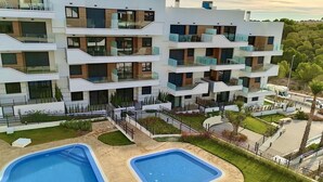 A modern multi-story residential building with balconies, a swimming pool, and a landscaped garden. - Luxe Appartement Orihuela-costa With Pool View (Orihuela)