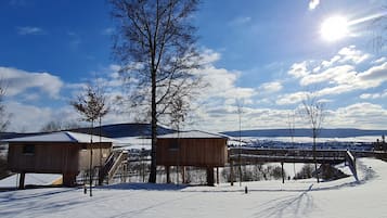 Eine Holzhütte mit einer Treppe, die zu einer Terrasse führt, umgeben von verschneitem Gelände und einem klaren Himmel.
