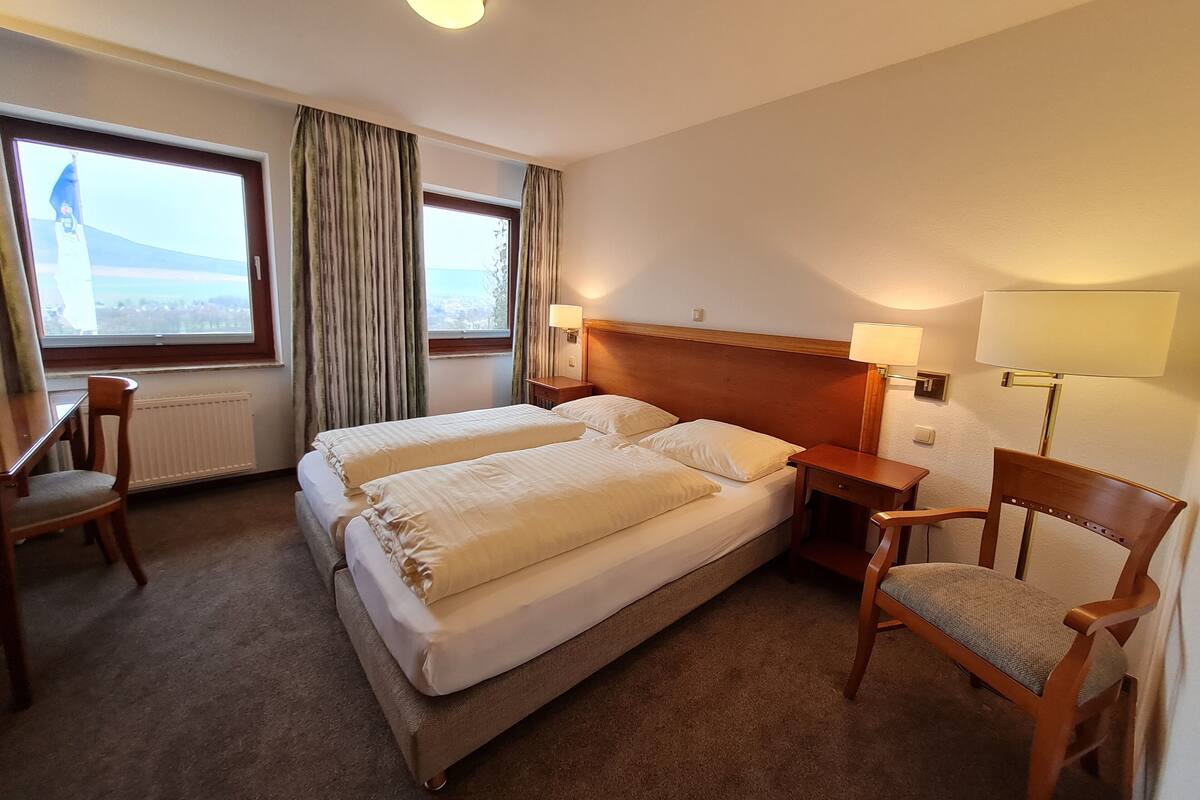 Ein Hotelzimmer mit zwei Betten, einem Schreibtisch, einem Stuhl, einer Lampe und Blick ins Freie.