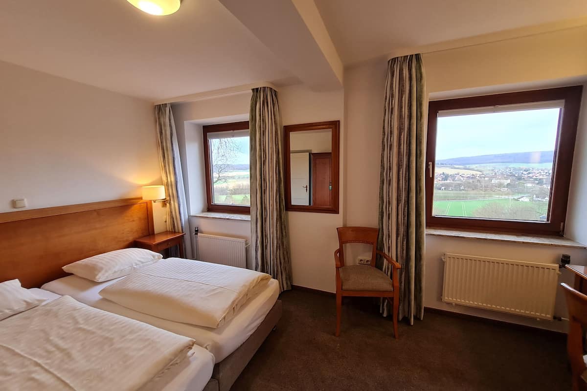 Ein Hotelzimmer mit zwei Betten, einem Sessel, einem Fenster mit Blick auf eine Stadt und einer Heizung.