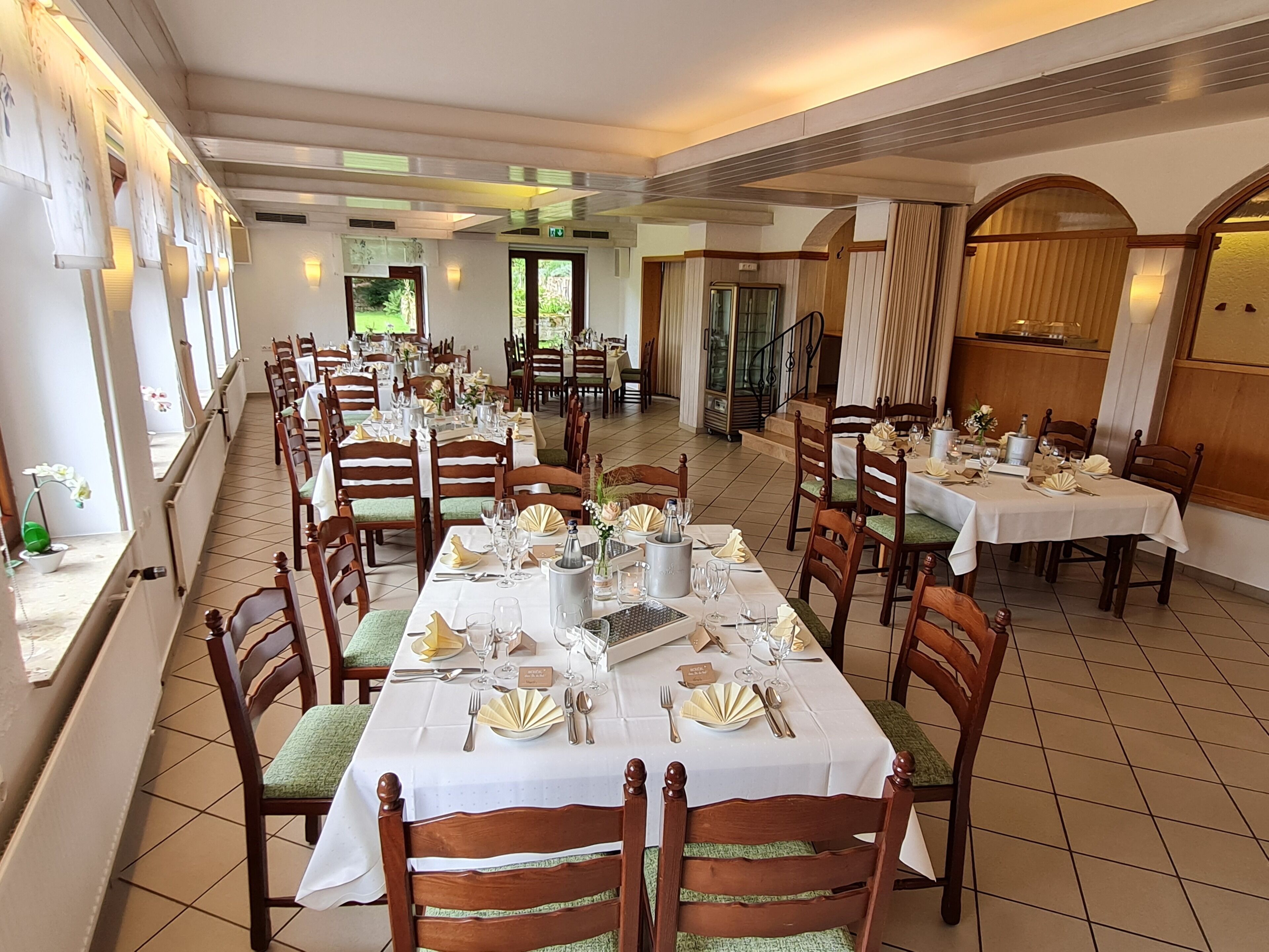 A dining area with multiple tables set for service, wooden chairs, and a tiled floor.