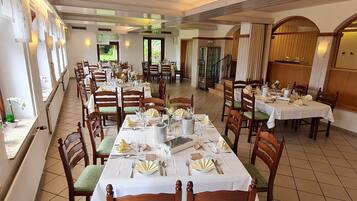 A dining area with multiple tables set for service, wooden chairs, and a tiled floor.