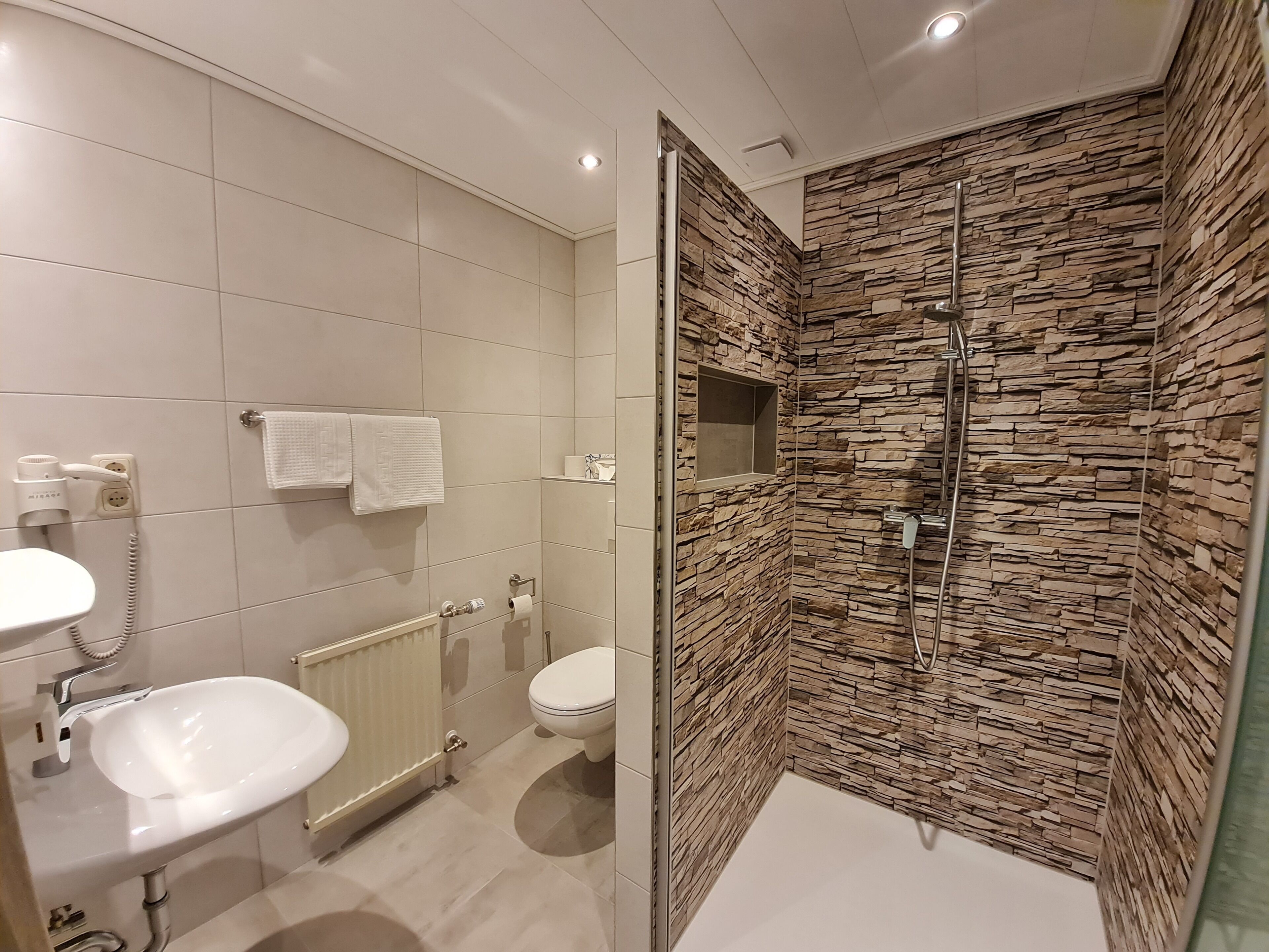 A modern bathroom with a white sink, toilet, and shower area.