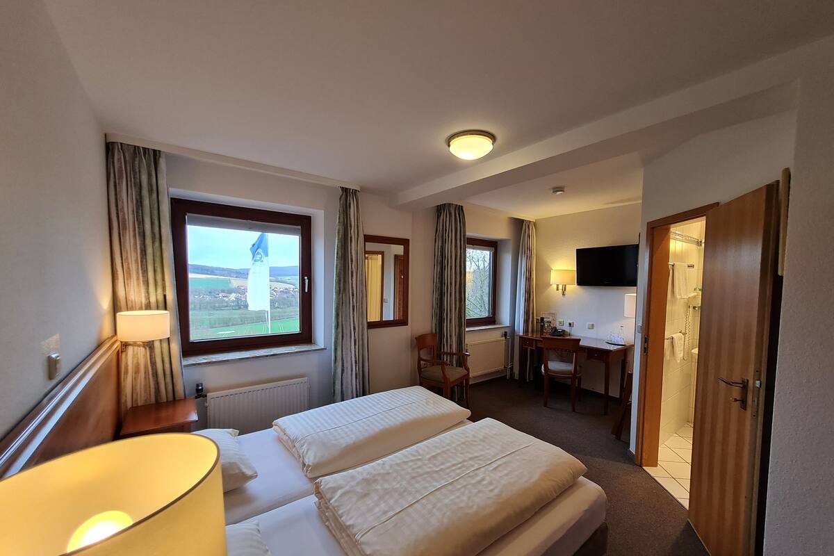 Ein Hotelzimmer mit Bett, Schreibtisch, Stuhl, Fernseher und einem Fenster mit Vorhängen.