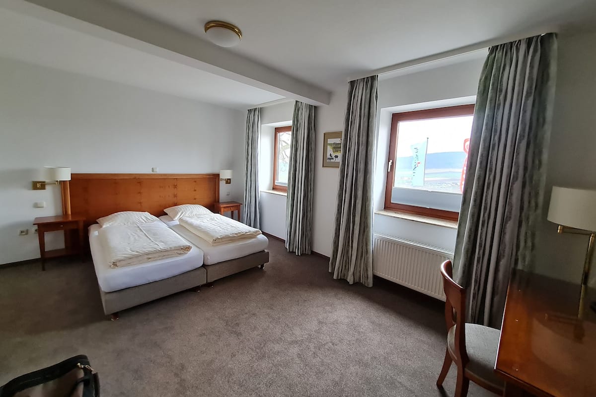 Ein Hotelzimmer mit zwei Betten, einem Fenster mit Vorhängen, einem Heizkörper und einem Sessel.