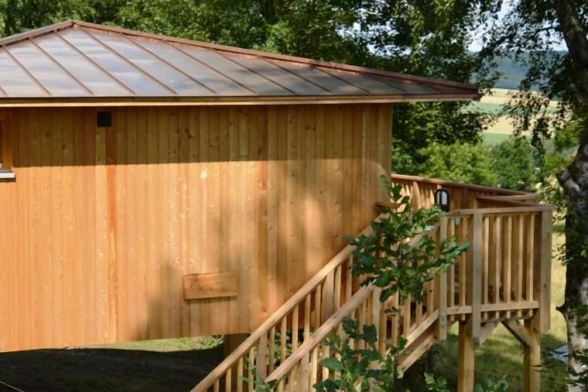 Eine Holzhütte mit einem Metalldach, einem kleinen Fenster und einer Holztreppe, die zu einer Terrasse führt.