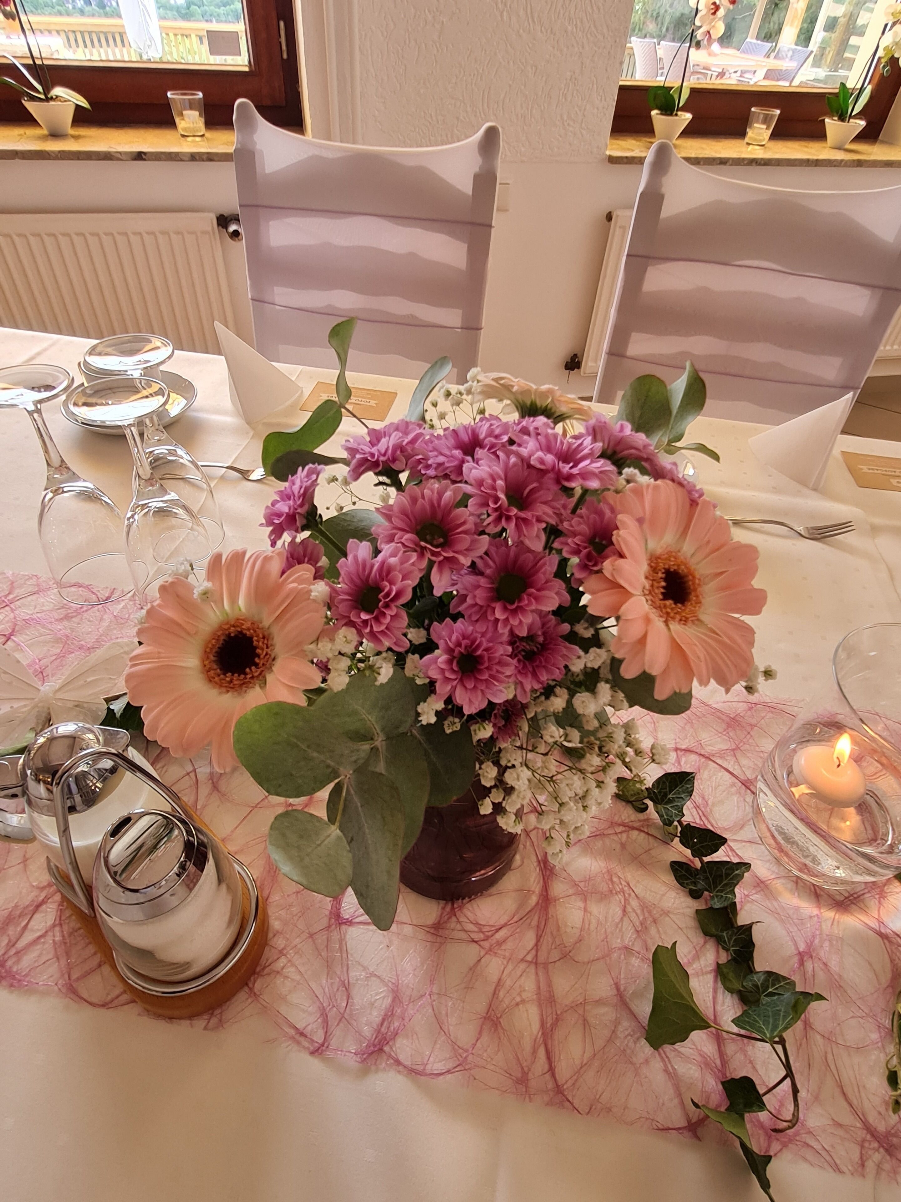 Una mesa de comedor dispuesta con un centro de mesa floral, copas de vino y una vela.