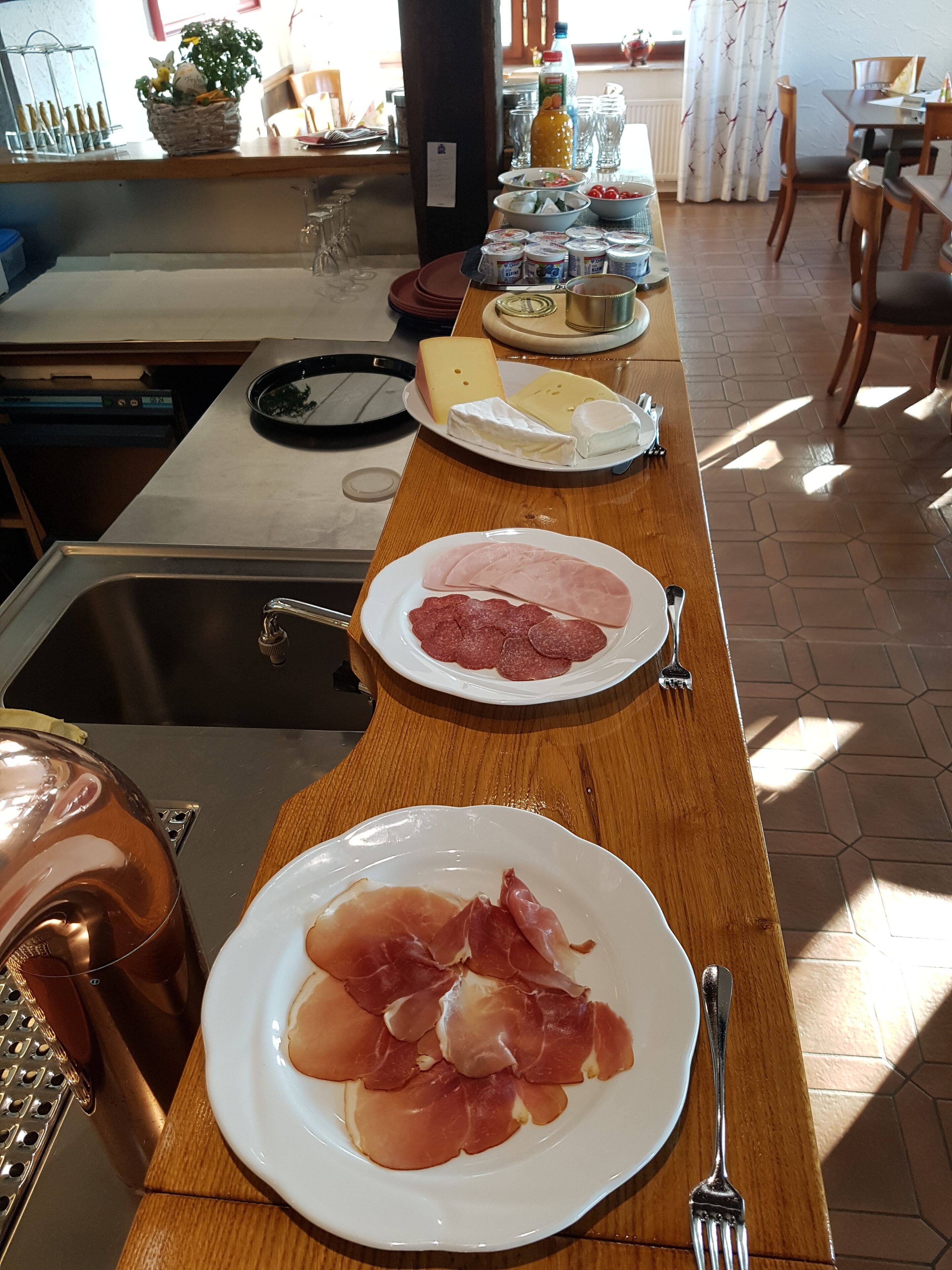 Un bufé de desayuno con platos de queso, jamón y prosciutto.