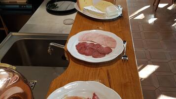 Un bufé de desayuno con platos de queso, jamón y prosciutto.