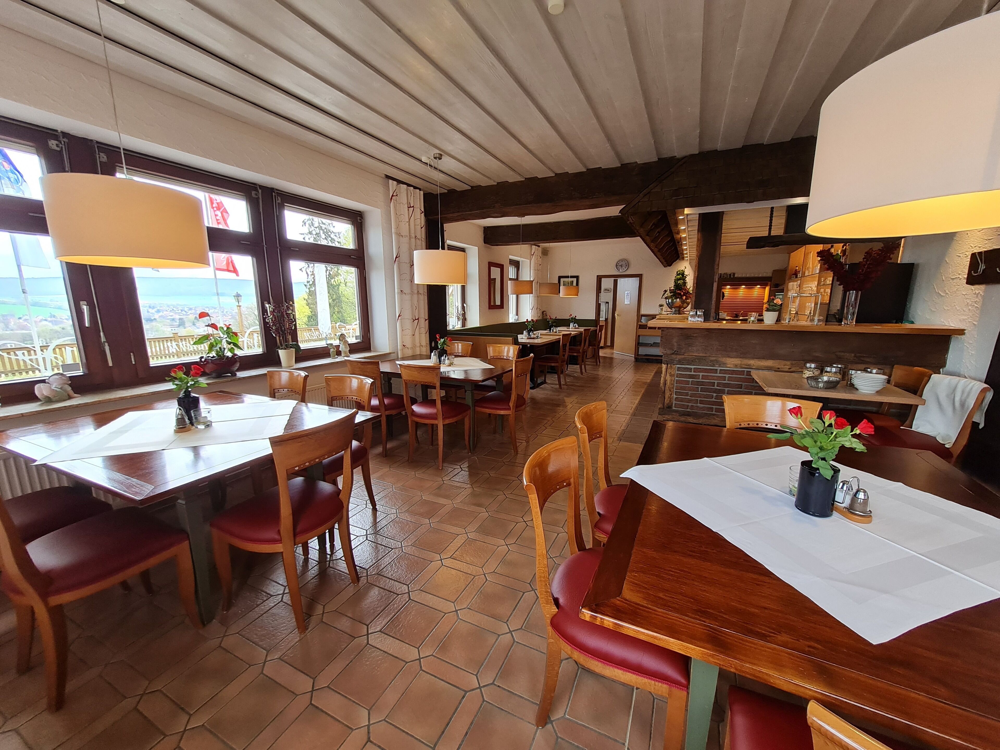 A restaurant with wooden tables and chairs, large windows, and a brick fireplace.