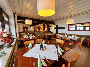 A restaurant with wooden tables and chairs, a bar area, and a flower arrangement on the counter. - Hotel Waldquelle - Baumhaushotel Aerzen (Aerzen)