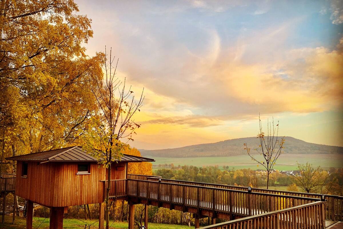 Eine Holzhütte mit einer Veranda, umgeben von Bäumen und Blick auf eine entfernte Landschaft.