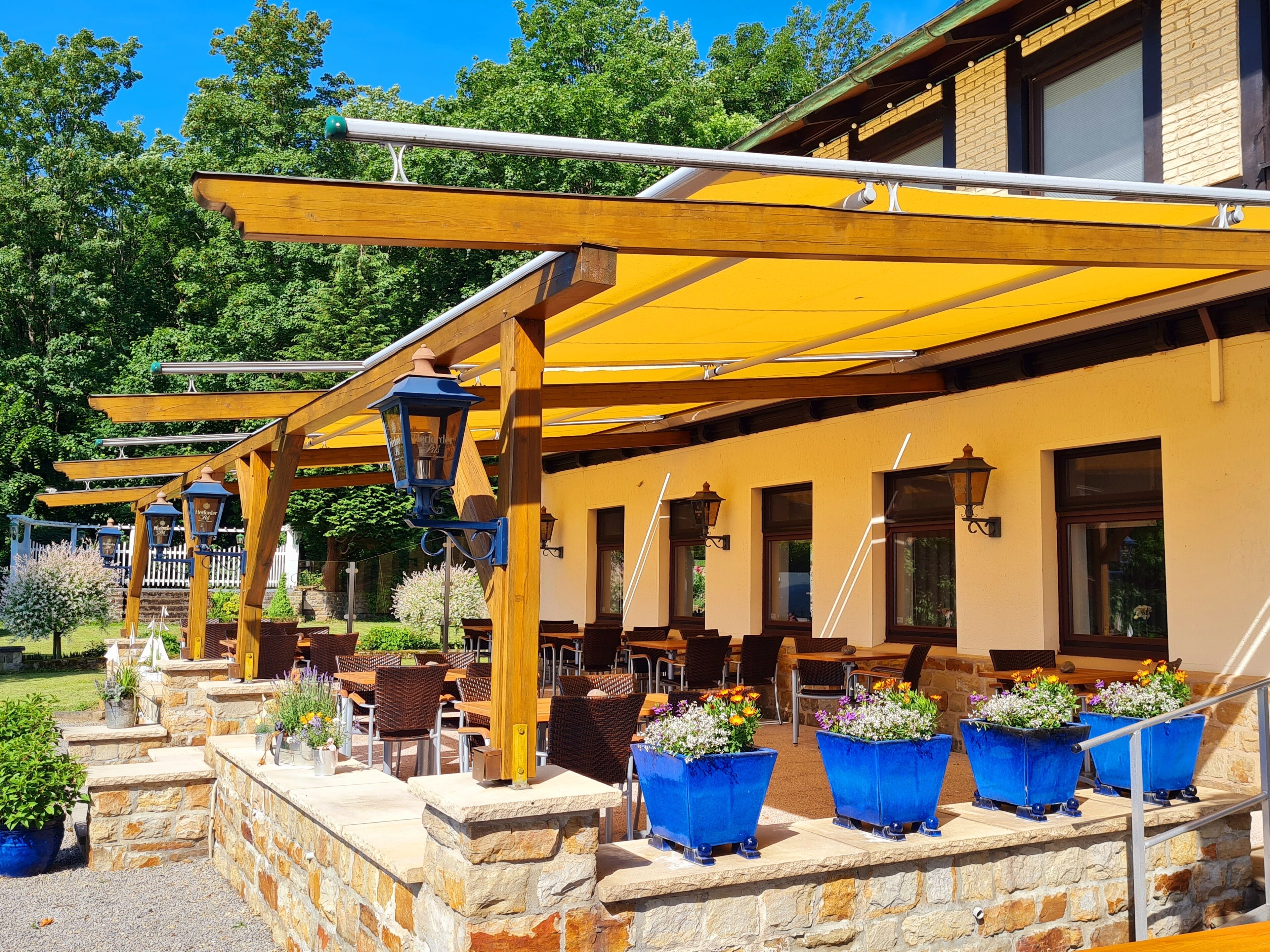 Un patio al aire libre con pérgolas de madera, paredes de piedra y macetas de flores azules.