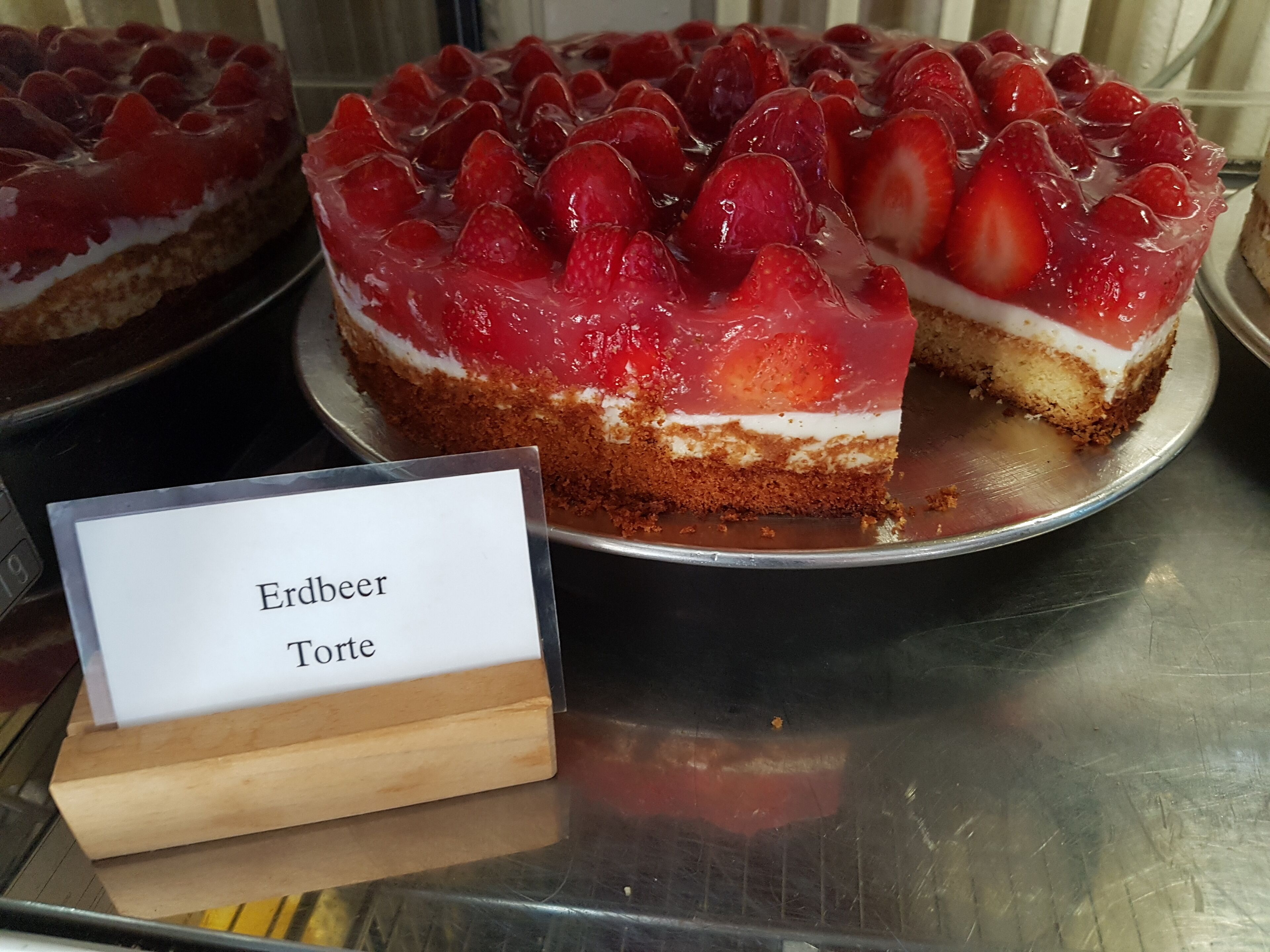 Mansikoilla koristeltu kakku, jonka kyljessä on kyltti, jossa lukee: ”Erdbeer Torte”.