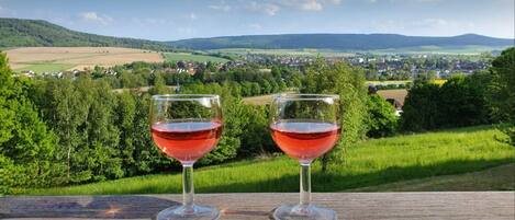 Dos copas de vino sobre una superficie de madera, con una vista panorámica de un pueblo y colinas al fondo.