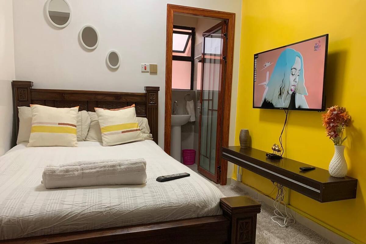 Une chambre à coucher avec un lit, une télévision, un miroir et une petite table sur laquelle se trouve un vase.