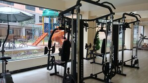 A gym with exercise equipment, a window view of a playground, and a wooden floor. - Lux Suites Kileleshwa Studio Apartments (Nairobi)