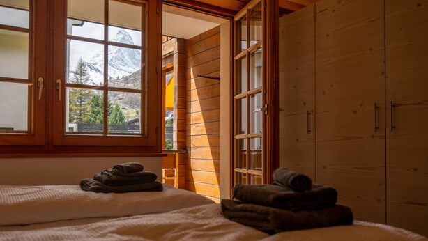 A room with two beds, a wooden wardrobe, and a window with a mountain view. - Baccara Studio  (Zermatt)