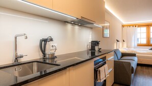 A compact kitchen with a sink, stove, and modern appliances. There is a sofa and a bed in the adjacent room. - Baccara Studio  (Zermatt)