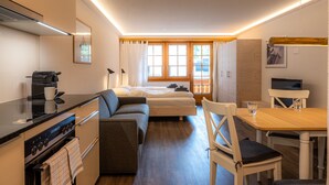 A compact room with a kitchenette, a bed, a dining table, and a TV. - Baccara Studio  (Zermatt)