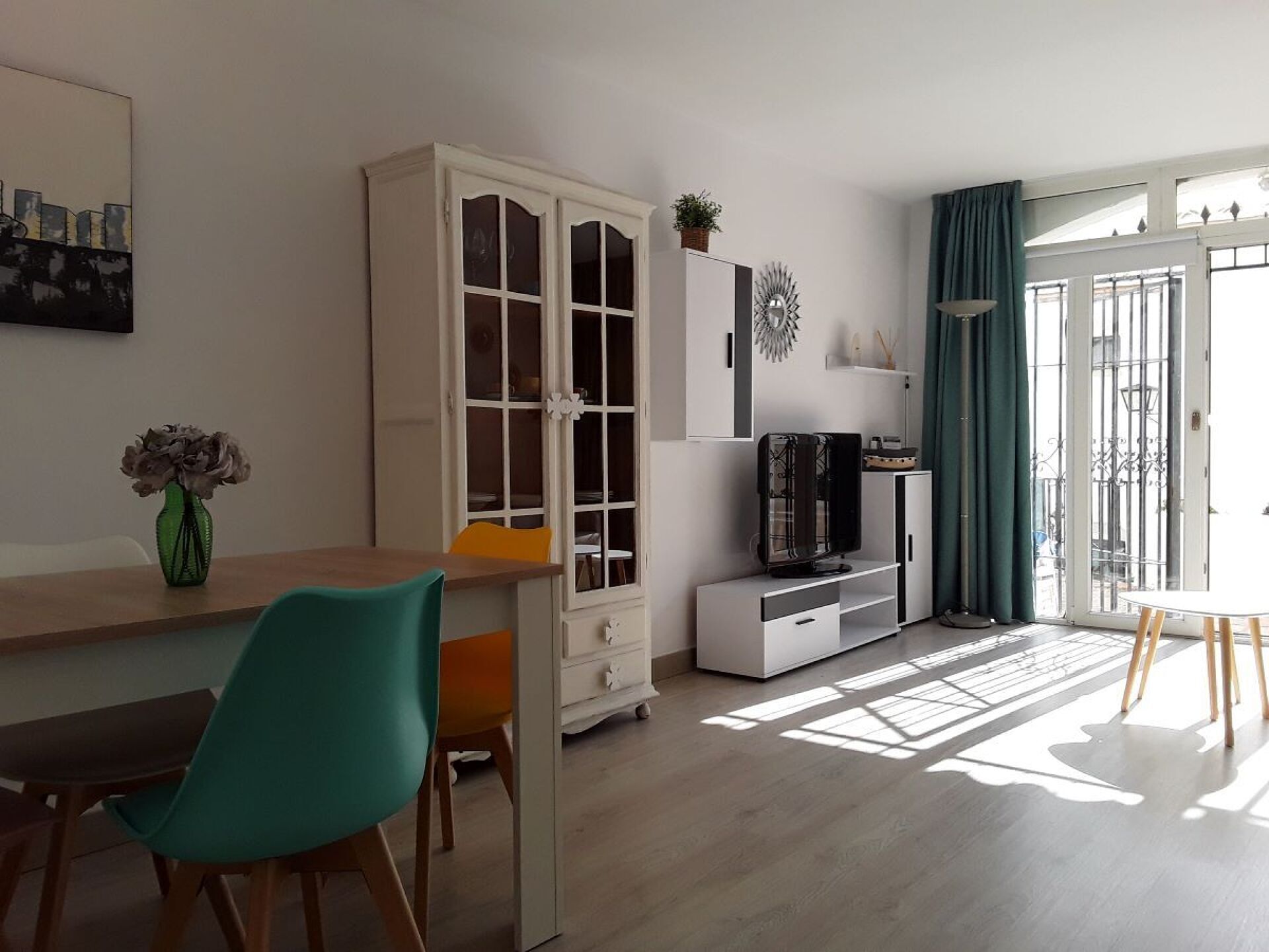 Uma sala de estar moderna com área de jantar, um armário grande, televisão e vista através de uma porta de vidro.