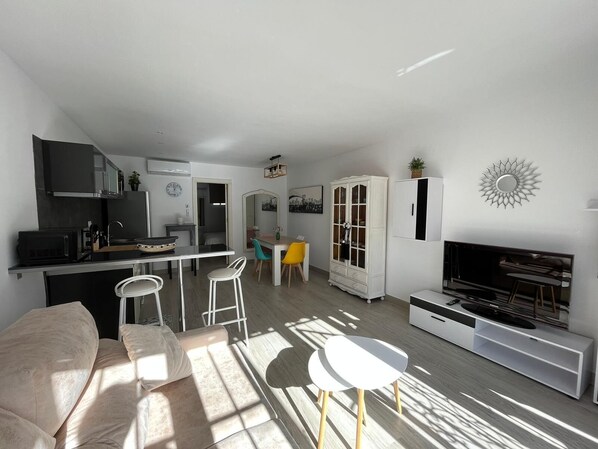 A modern living room with a sofa, a TV, a dining area, and a kitchen.
