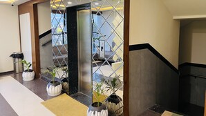 Un moderno vestíbulo de hotel con un separador de vidrio geométrico, plantas en macetas y vistas panorámicas de la ciudad a través de grandes ventanales.
