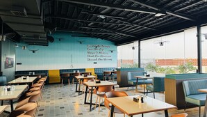 Un interior de restaurante con cabinas y mesas, una pared azul con texto y ventanas amplias.