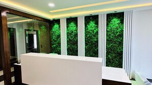 Un área de recepción con un mostrador blanco, columnas verticales y una pared iluminada en verde.