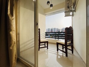 A balcony with two wooden chairs, a view of buildings, and a window with blinds. - Hotel Shree Palace (Ujjain)
