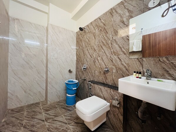 A bathroom with a marble wall, a white sink, a mirror, and a shower. - Hotel Shree Palace (Ujjain)