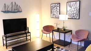 A modern living room with a flat-screen TV, two pink chairs, a coffee table, and two abstract wall art pieces. - Cozy Home in Frisco/Little Elm (Little Elm)
