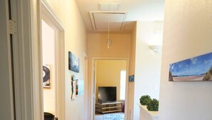 A hallway with a carpeted floor, white walls, and a ceiling light. There are framed pictures on the walls and a door on the left. - Cozy Home in Frisco/Little Elm (Little Elm)