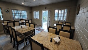 A dining area with multiple tables and chairs, a ceiling fan, and large windows with bars. - Ibex Resorts, Valparai (Mistly) (Valparai)