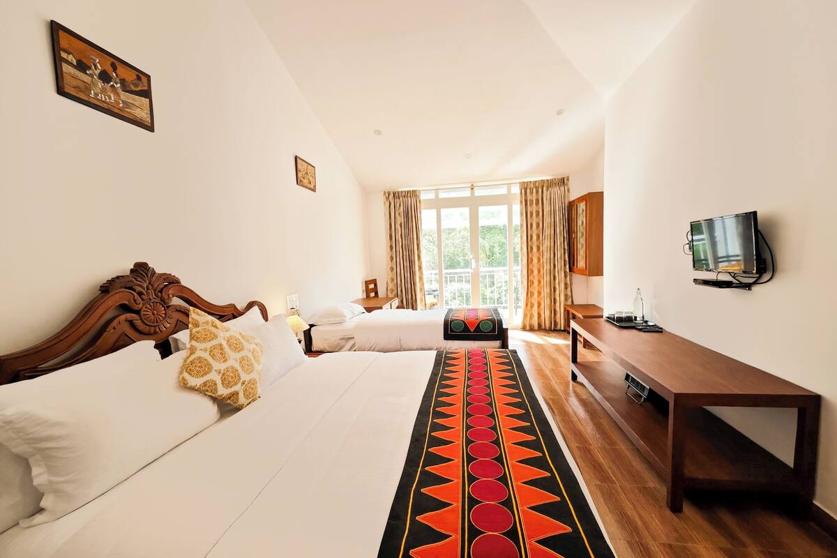 Une chambre d’hôtel avec deux lits, une télévision, un bureau et une fenêtre avec des rideaux.