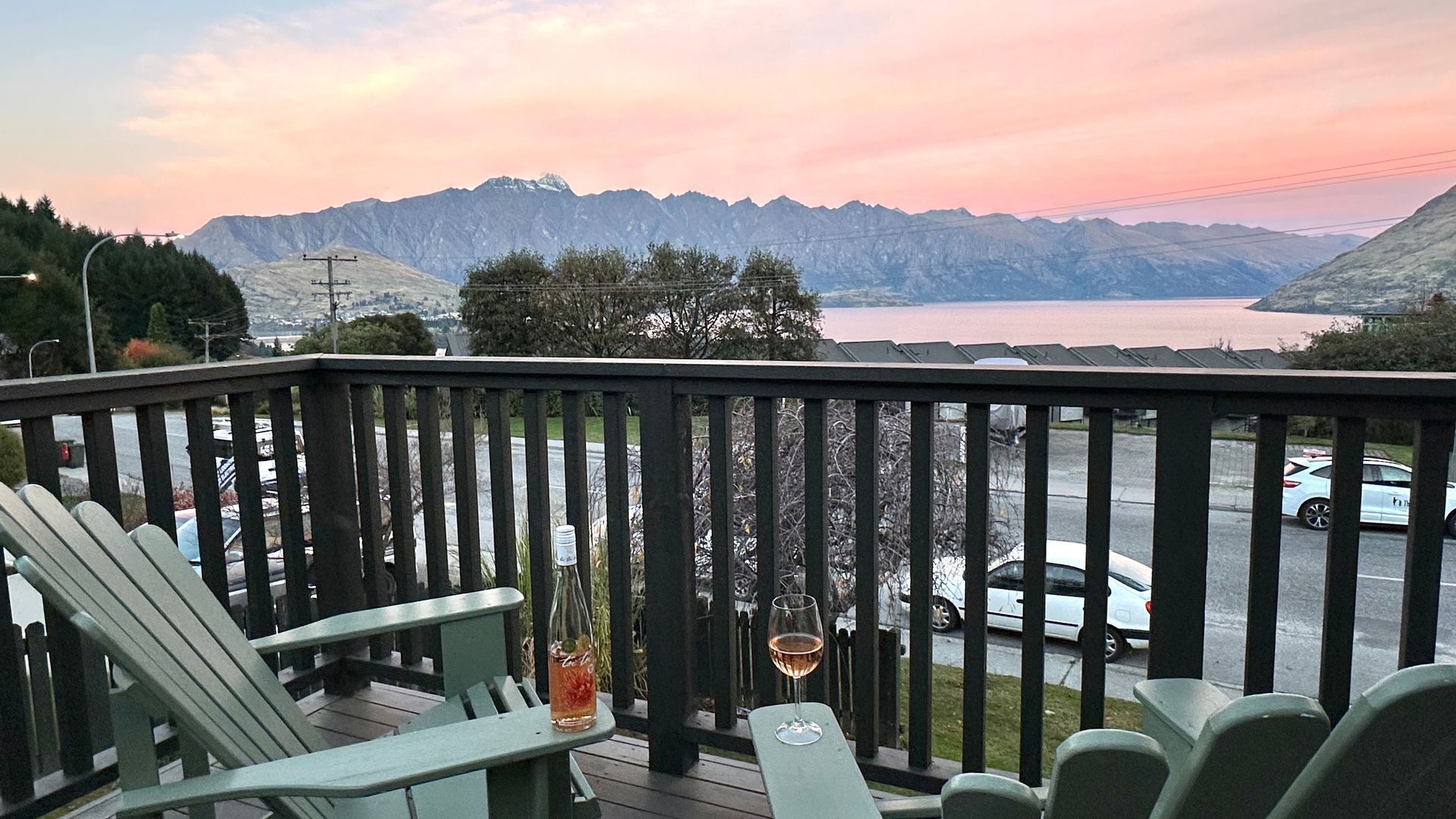 A balcony with chairs and a table, overlooking a lake and mountains.