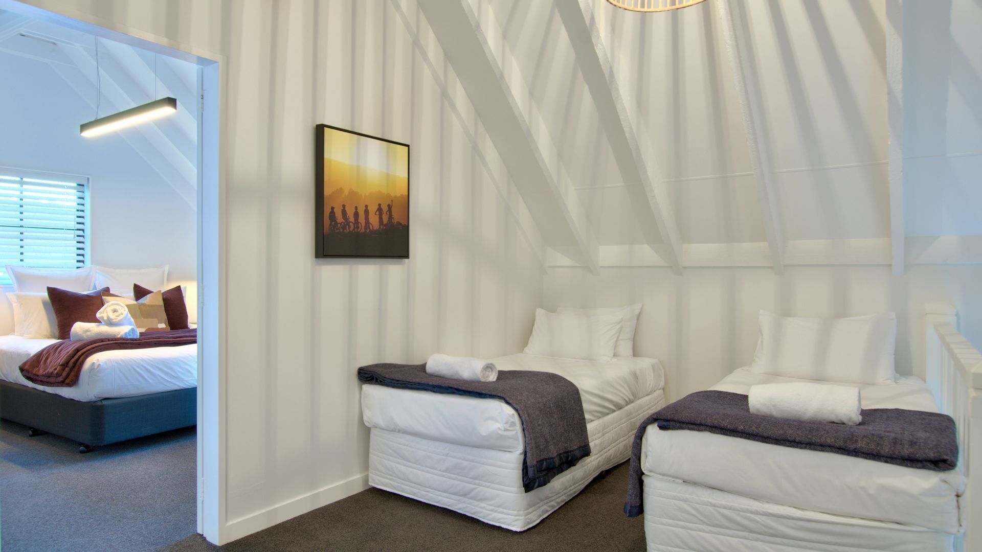Una habitación de hotel moderna con un diseño de techo único tipo tienda, dos camas, un cuadro en la pared y vistas al exterior.
