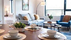 En moderne stue med et spisebord dækket til to, en sofa, en blå lænestol og et stort vindue med udsigt.