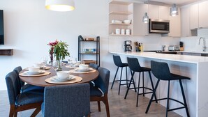 Et moderne køkken med hvide skabe, en central ø med barstole og et spiseområde med et rundt bord og stole.