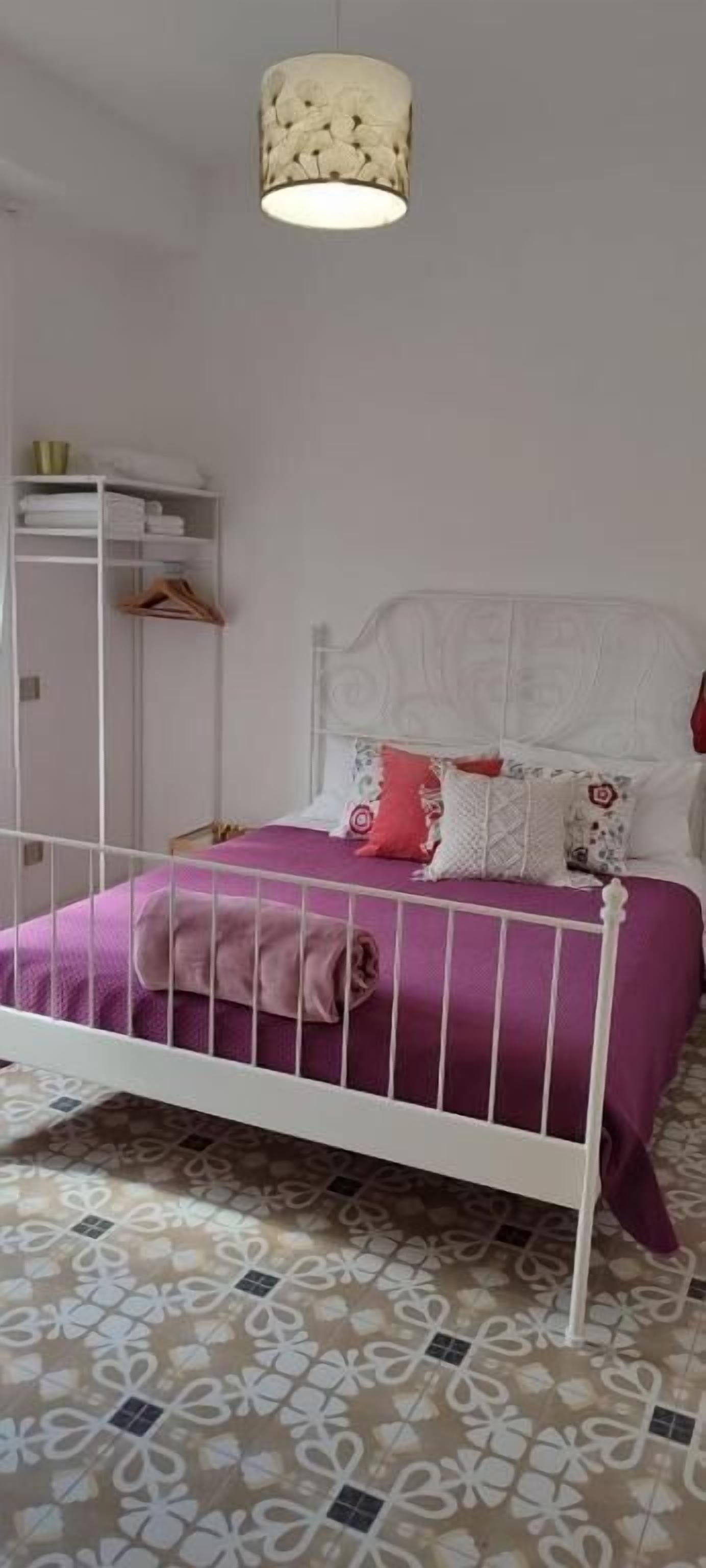 A bedroom with a white metal bed frame, a purple bedspread, and a hanging light fixture.
