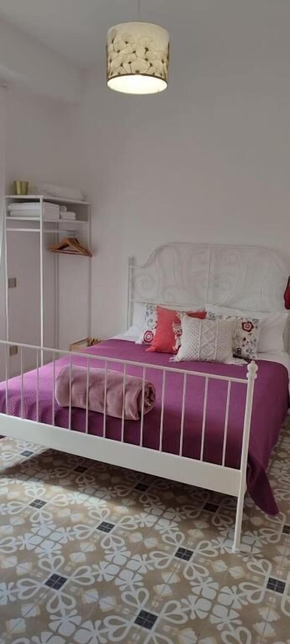 Une chambre à coucher avec un lit en métal blanc, une couvre-lit violette et un luminaire suspendu.