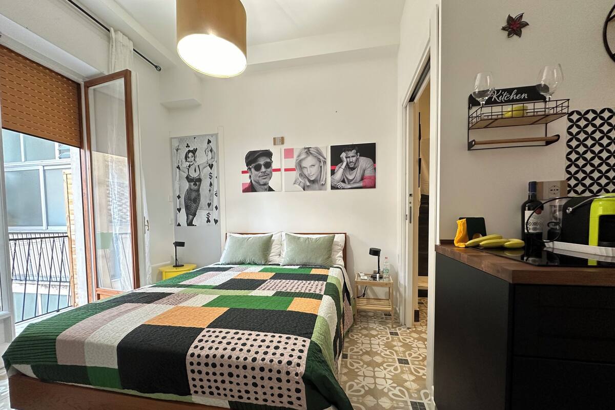 A bedroom with a bed, a nightstand, a desk, and a window with blinds.