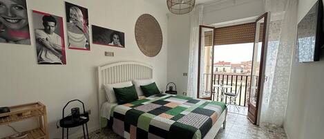 Un dormitorio con cama, mesita de madera, aire acondicionado de pared y balcón con vistas.