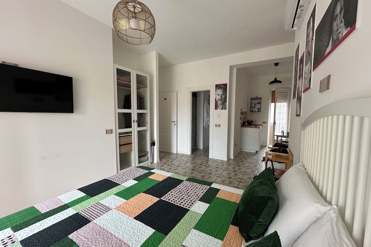A bedroom with a large bed, a wardrobe, a kitchen area, and a hallway.