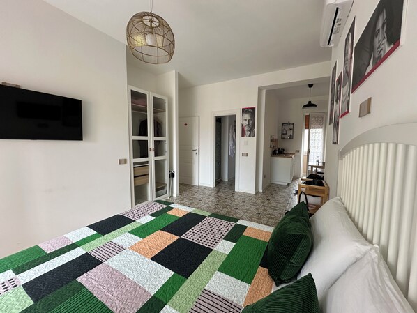 A bedroom with a large bed, a wardrobe, a kitchen area, and a hallway.