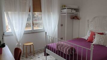 A bedroom with a bed, a window with curtains, a bedside table, a chair, and a wardrobe.