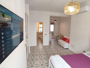 A hotel room with a bed, a sofa, a desk, and a TV displaying a guide.