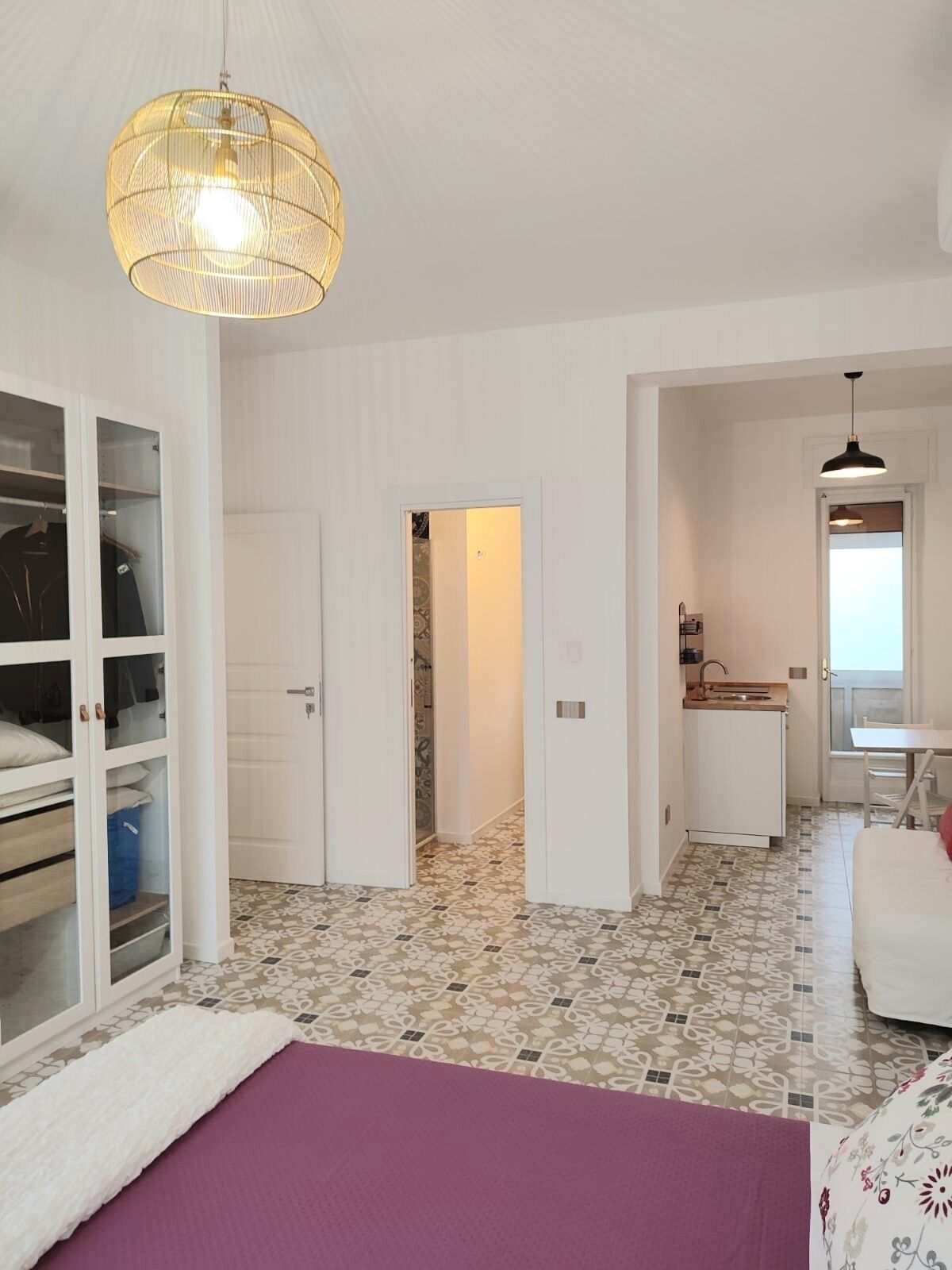 A bedroom with a bed, a wardrobe, a hanging light fixture, and a bathroom visible through an open door.