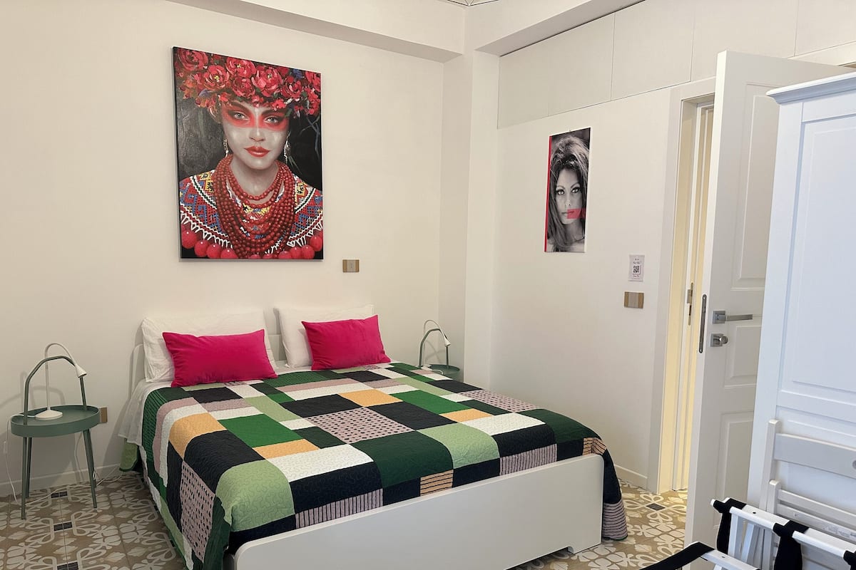 A bedroom with a bed, two nightstands, a wall-mounted painting, and a door.